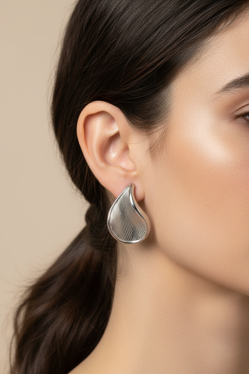 Silver wave drop stainless steel earrings worn on ear close up jewelry
