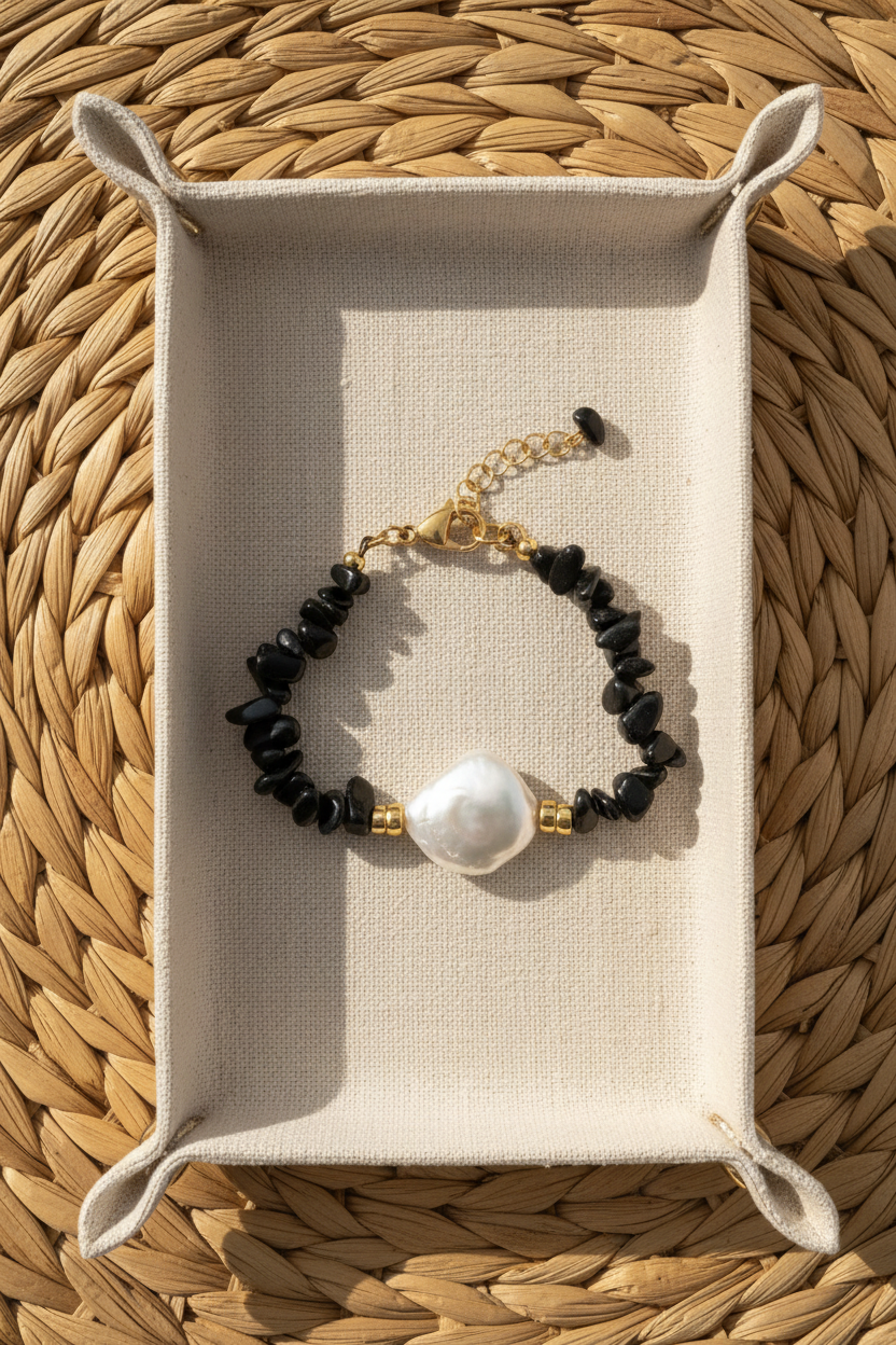 Black beaded bracelet with a pearl on a beige jewelry tray, placed on a woven surface.