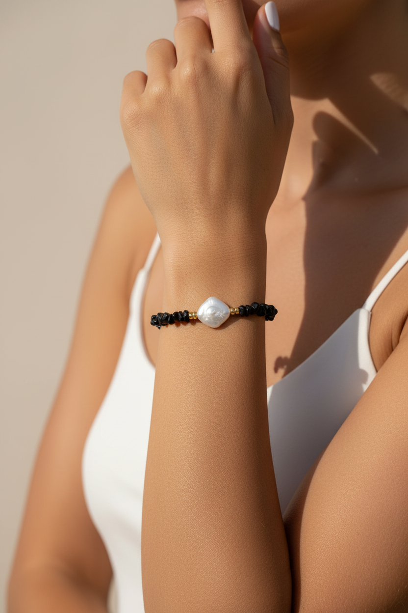 Close-up of a hand wearing a bracelet with a pearl on a neutral background