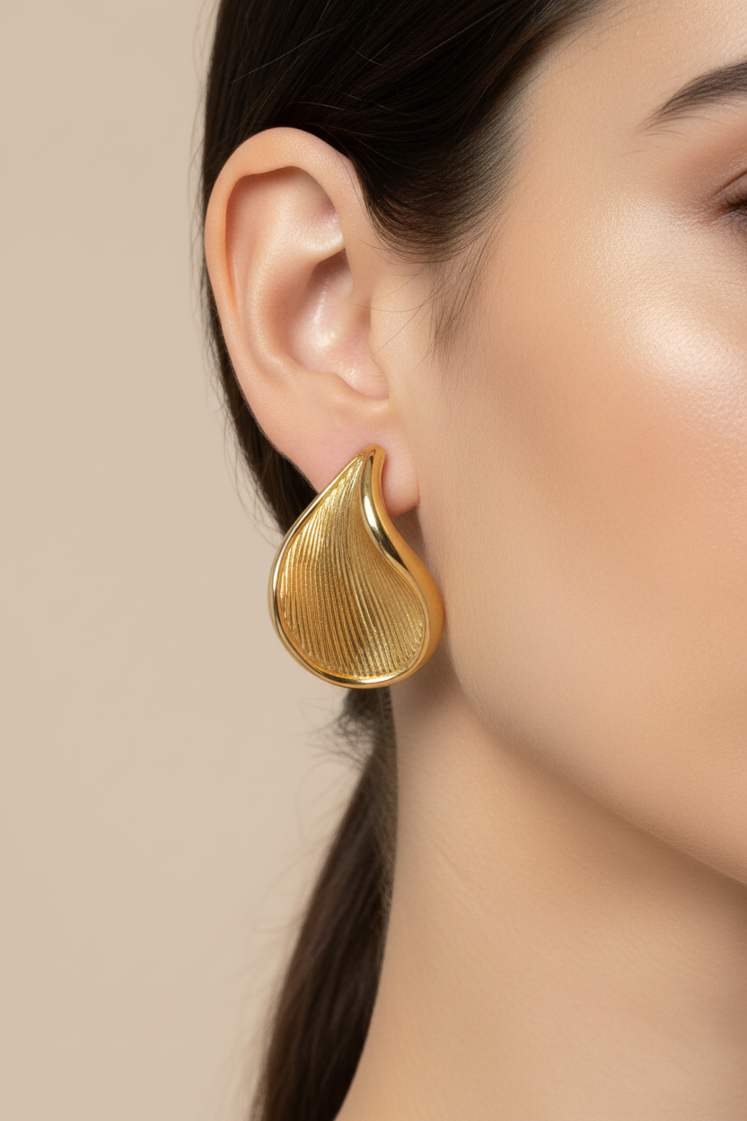Gold wave drop stainless steel earrings worn on ear close up jewelry
