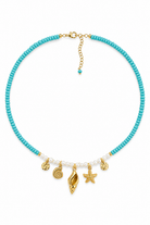 A turquoise beaded necklace with gold-tone charms shaped like a seashell, starfish, and seashells, accented by small white pearls, shown on a plain white background.