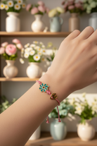 Bracelet with a floral design worn on a wrist, with a blurred background of flowers and vases.