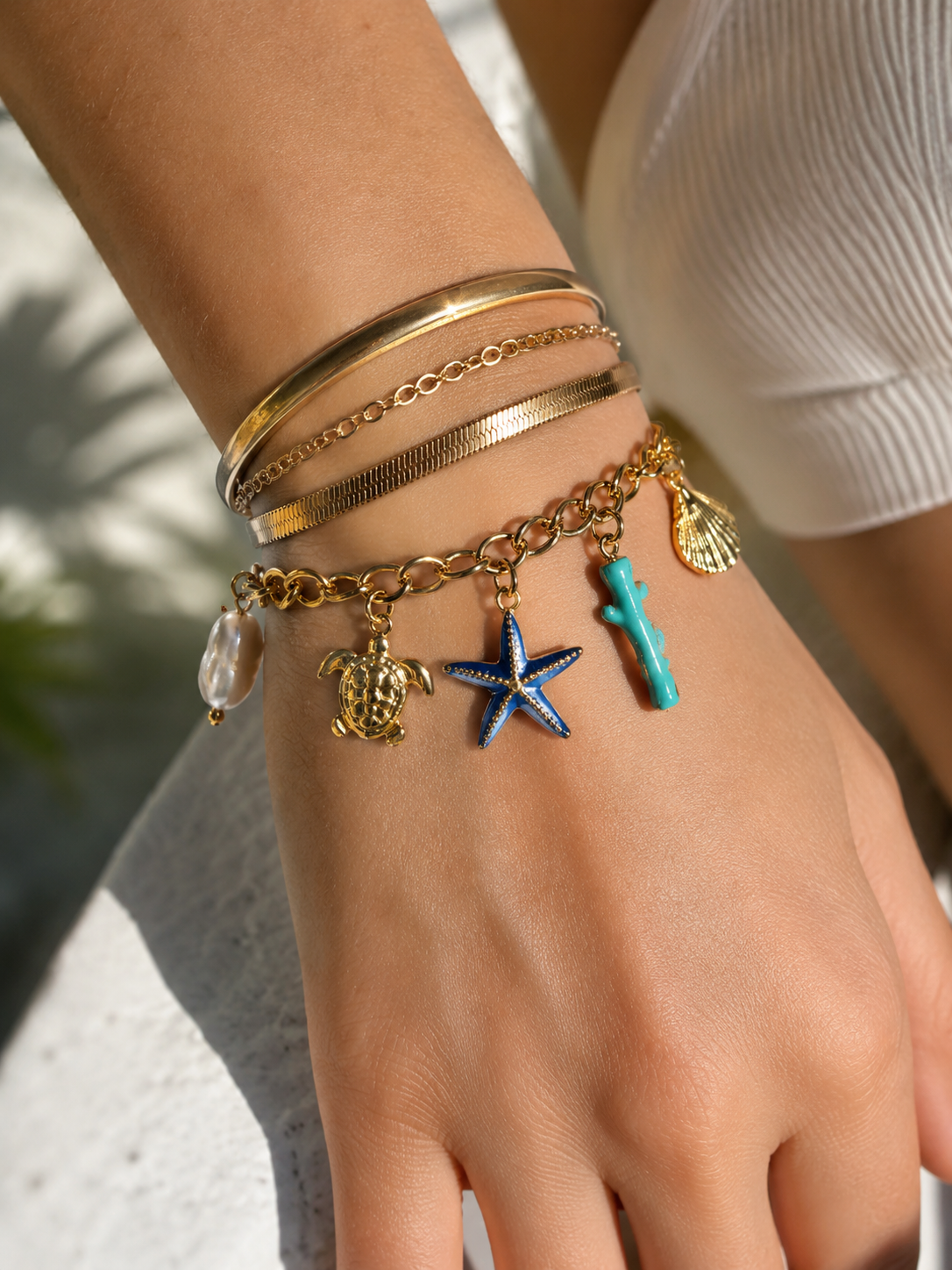 Hand wearing multiple gold bracelets with various charms against a blurred background