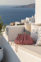 Ψάθινο clutch bag με χρυσό frame και αποσπώμενη αλυσίδα σε ροζ  απόχρωση σε νησιώτικο σκηνικό – So Cute by Dimi
