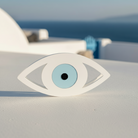 Decorative eye-shaped object on a white surface with a blue sky and ocean in the background