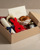 Easter gift box with bunny, candle, and bread on a neutral background