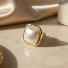 Gold ring with a large pearl on a beige marble surface