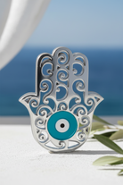 Silver Hamsa hand with turquoise eye against a blurred natural background
