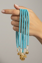 Hand holding multiple turquoise beaded necklaces with gold accents against a neutral background