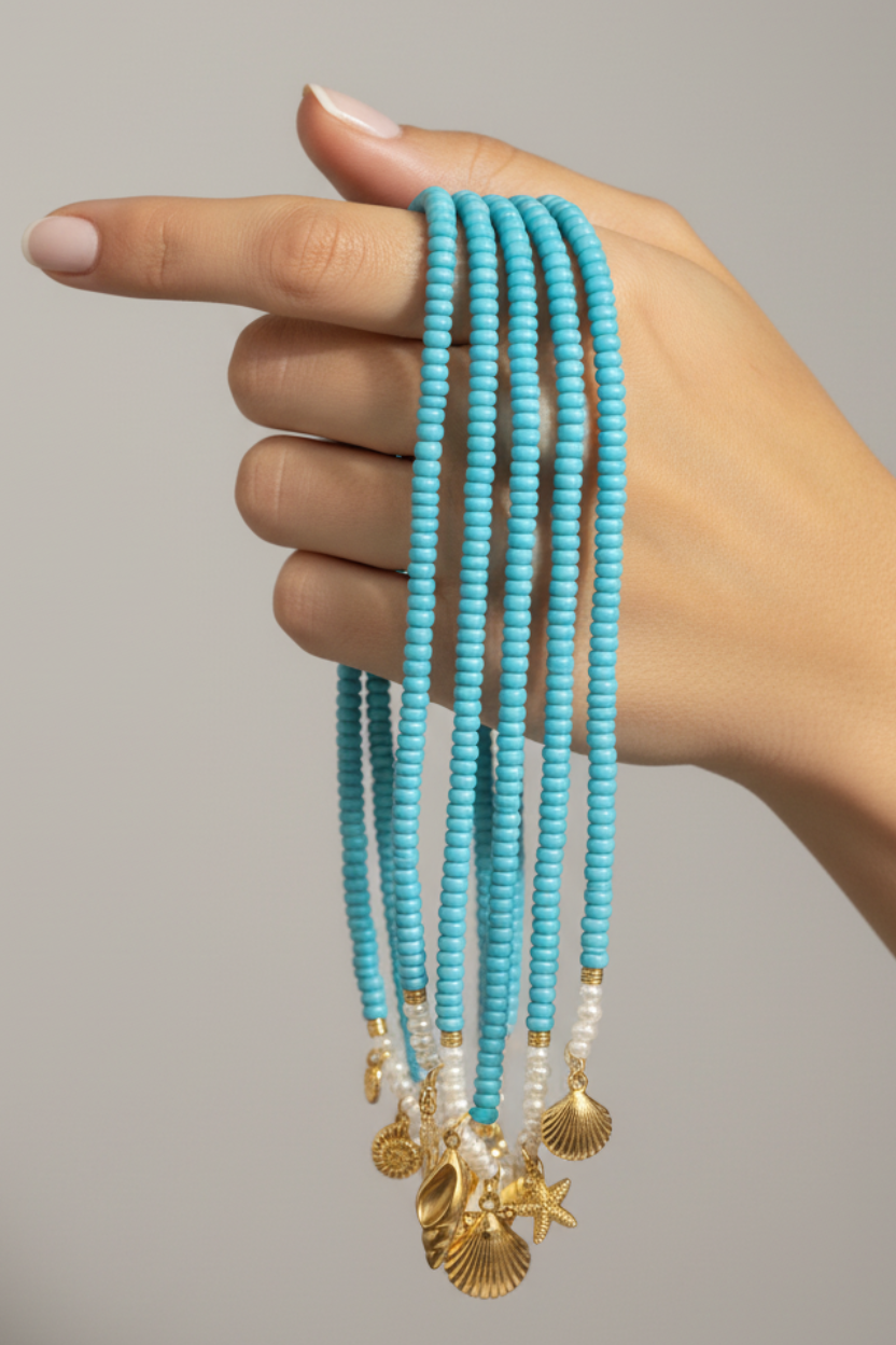 Hand holding multiple turquoise beaded necklaces with gold accents against a neutral background