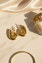 Gold hoop earrings on a beige fabric background with a perfume bottle.