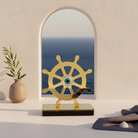 Decorative ship's wheel with a mirror reflecting ocean view on a shelf.