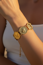 Gold bracelet with coin designs on a wrist against a blurred background