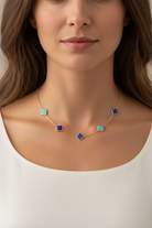 Woman wearing a gold necklace with blue gemstones on a plain background