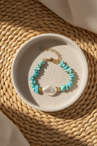 Turquoise beaded bracelet with a gold clasp on a beige dish, placed on a woven mat.