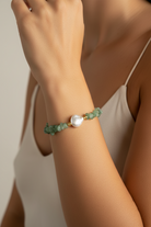 Bracelet with green beads and a pearl on a wrist, against a neutral background