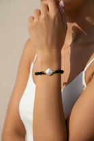 Close-up of a hand wearing a bracelet with a pearl on a neutral background
