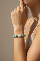 Bracelet with turquoise beads and a pearl worn on a wrist against a neutral background