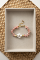 Pink beaded bracelet with a large pearl in a beige box on a woven surface
