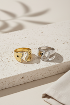 Curve Glow Ring σε χρυσό και ασημί χρώμα, ατσάλινο ανοιχτό δαχτυλίδι με ζιργκόν σε minimal flatlay