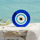 Αυτοστηριζόμενο μπλε ακρυλικό γούρι μάτι με τιρκουάζ λεπτομέρειες σε πέτρινη επιφάνεια δίπλα στη θάλασσα.