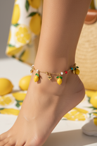 Anchored anklet with lemon charms on a foot, with lemons in the background