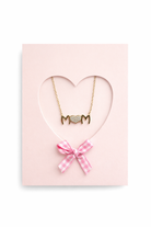 Gold necklace with 'MOM' pendant on a pink heart-shaped card with a pink bow.