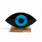 Decorative eye-shaped object with a blue center and black outer rim on a wooden stand, branded 'So Cute'.