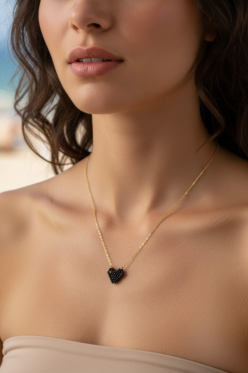 Close-up of a woman wearing a gold necklace with a black heart miyuki pendant.