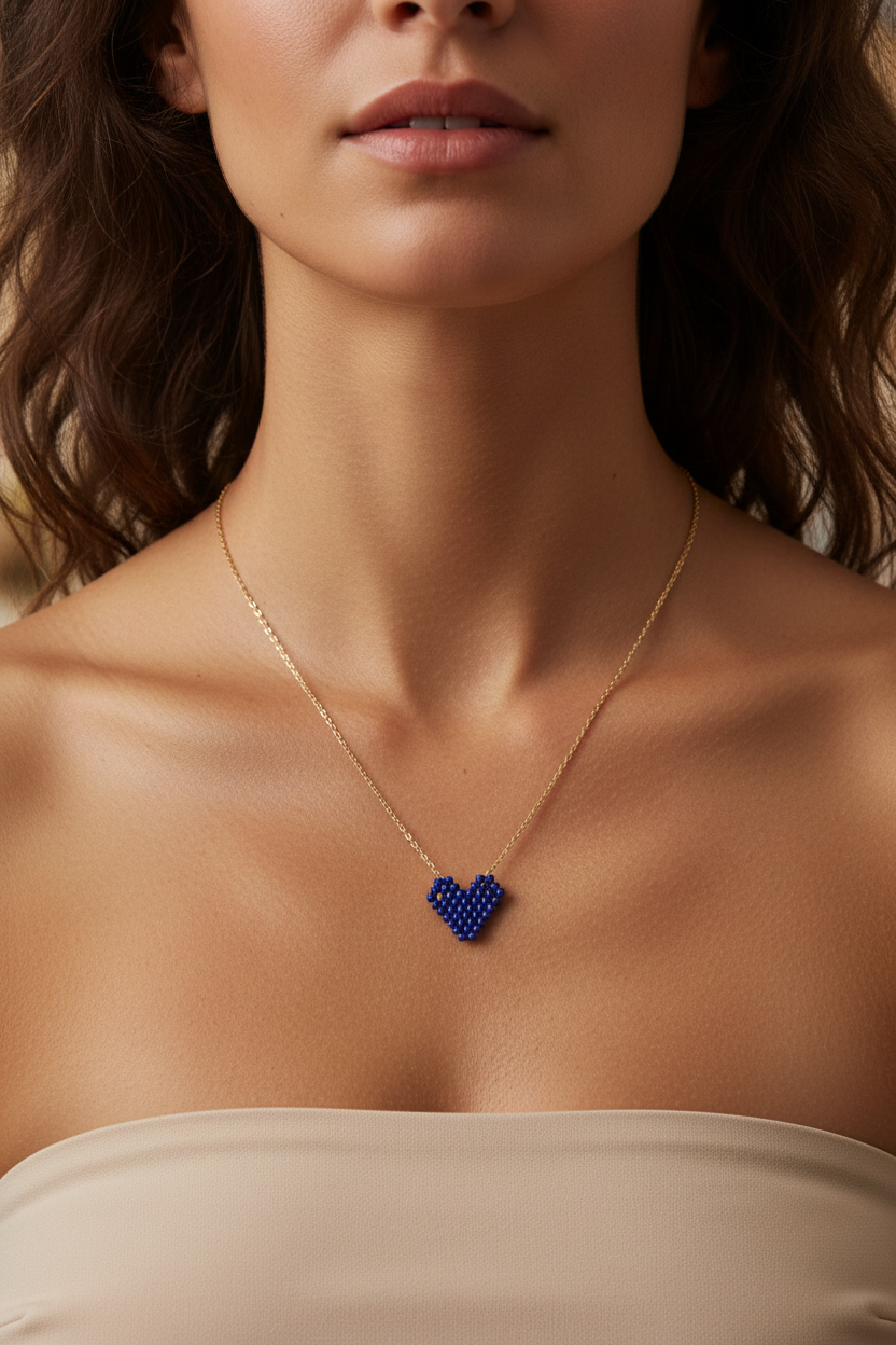 Close-up of a necklace with a blue heart miyuki pendant on a person wearing a beige top.