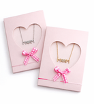 Two Mom necklaces in pink heart-shaped boxes with bows on a white background