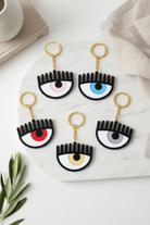 Eye-shaped keychains on a marble surface with a cup and plant in the background