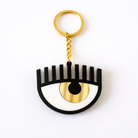 Keychain with eye design featuring a black half-circle and gold crescent moon on a white background