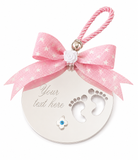 A personalized baby keepsake ornament featuring a round silver disc with footprints and text, adorned with a pink star-patterned ribbon bow and a hanging loop.