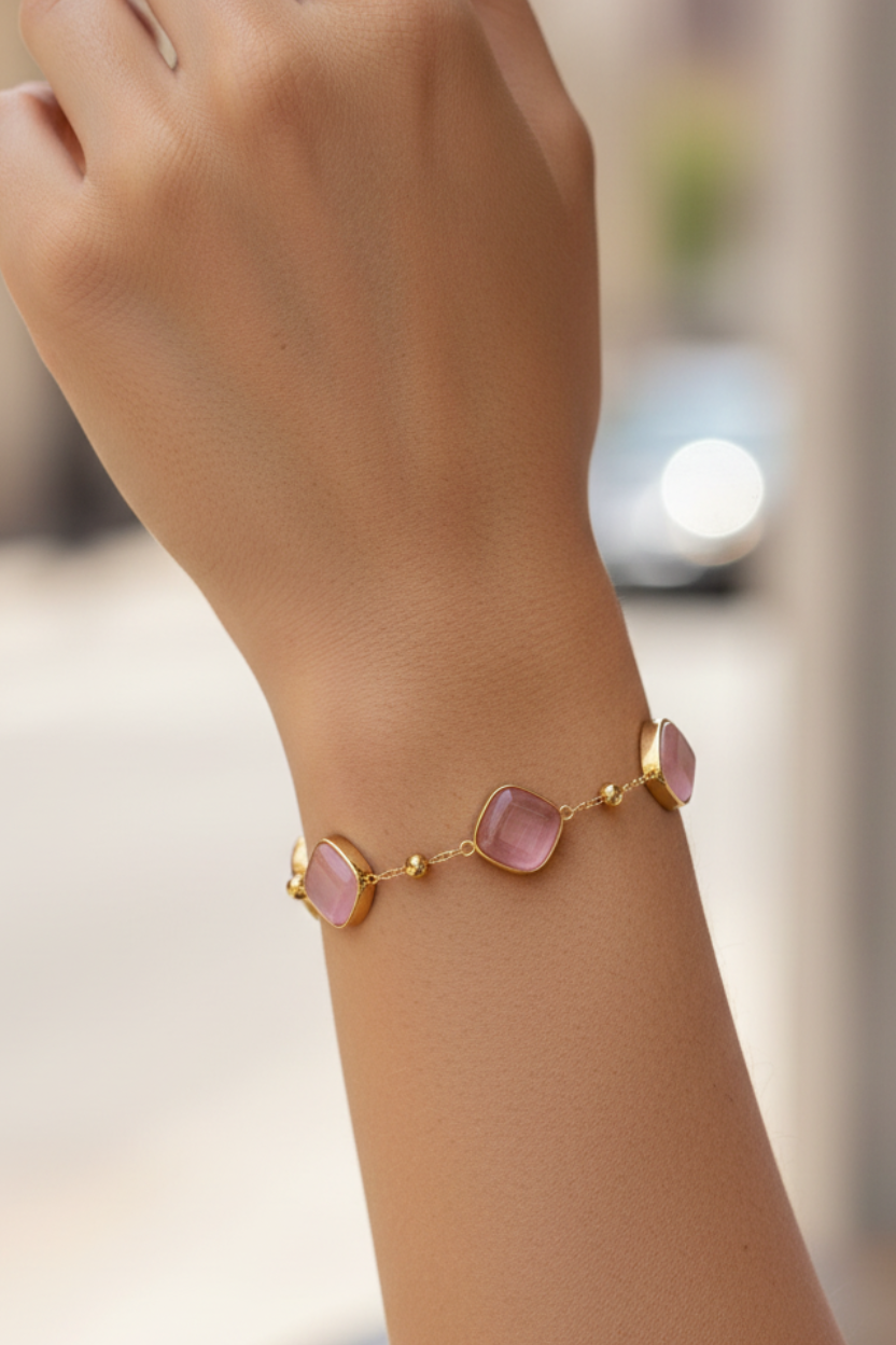 Hand wearing a gold bracelet with pink stones on a blurred background