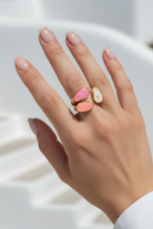 Hand wearing a ring with pink and gold design on a white background