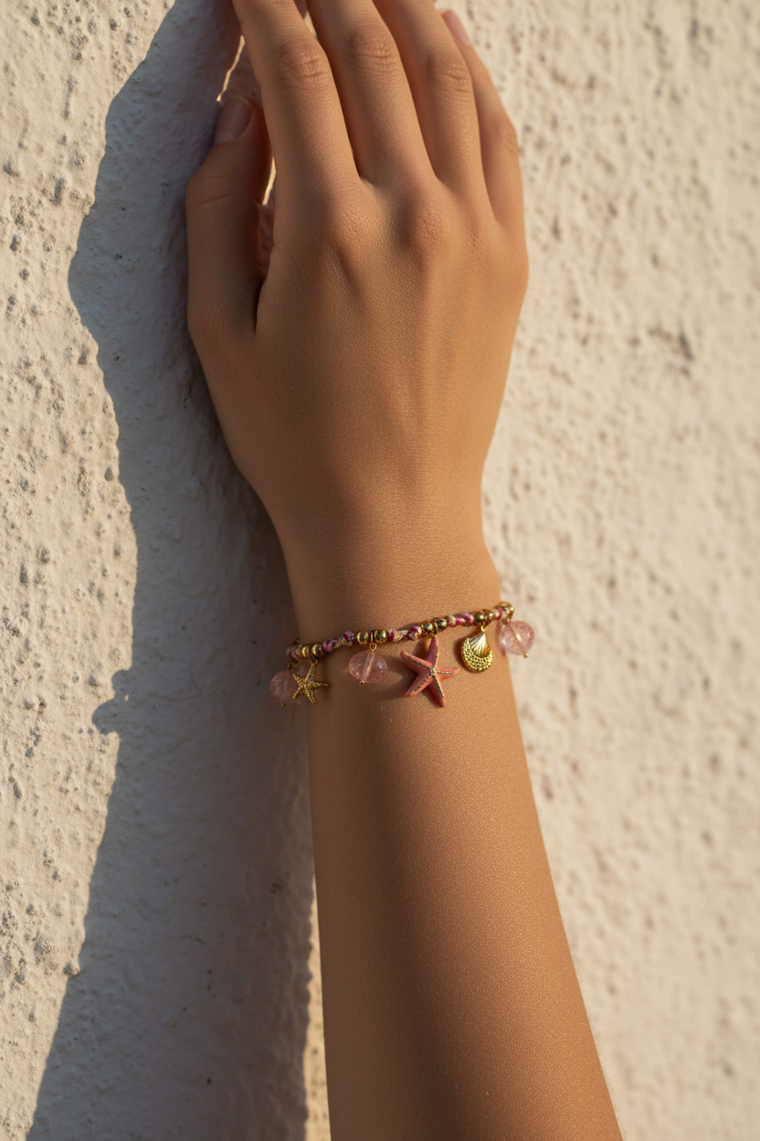 Hand wearing a bracelet with starfish charm against a textured wall, So cute by DImi