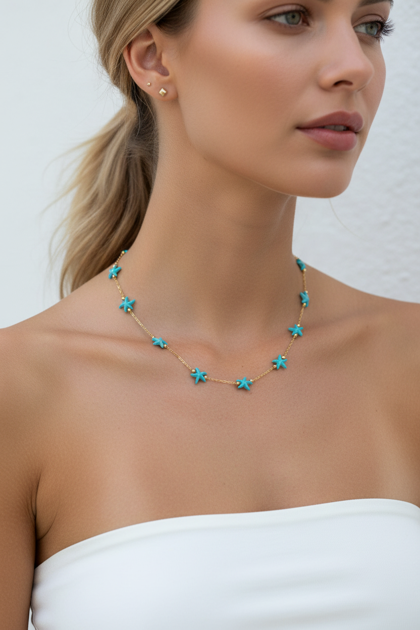A close-up of a woman wearing a delicate gold necklace with small turquoise star-shaped charms, paired with a white strapless top.
