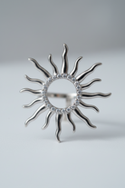 Silver sun-shaped ring with rhinestones on a light gray background