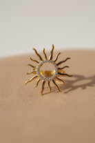 Gold sun-shaped ring with rhinestones on a beige background