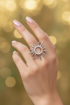 Silver sun-shaped ring on a hand with a blurred golden background