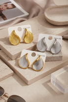 Wave drop stainless steel earrings gold silver two tone editorial jewelry flat lay
