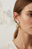 Close-up of a woman wearing gold and pearl earrings against a neutral background