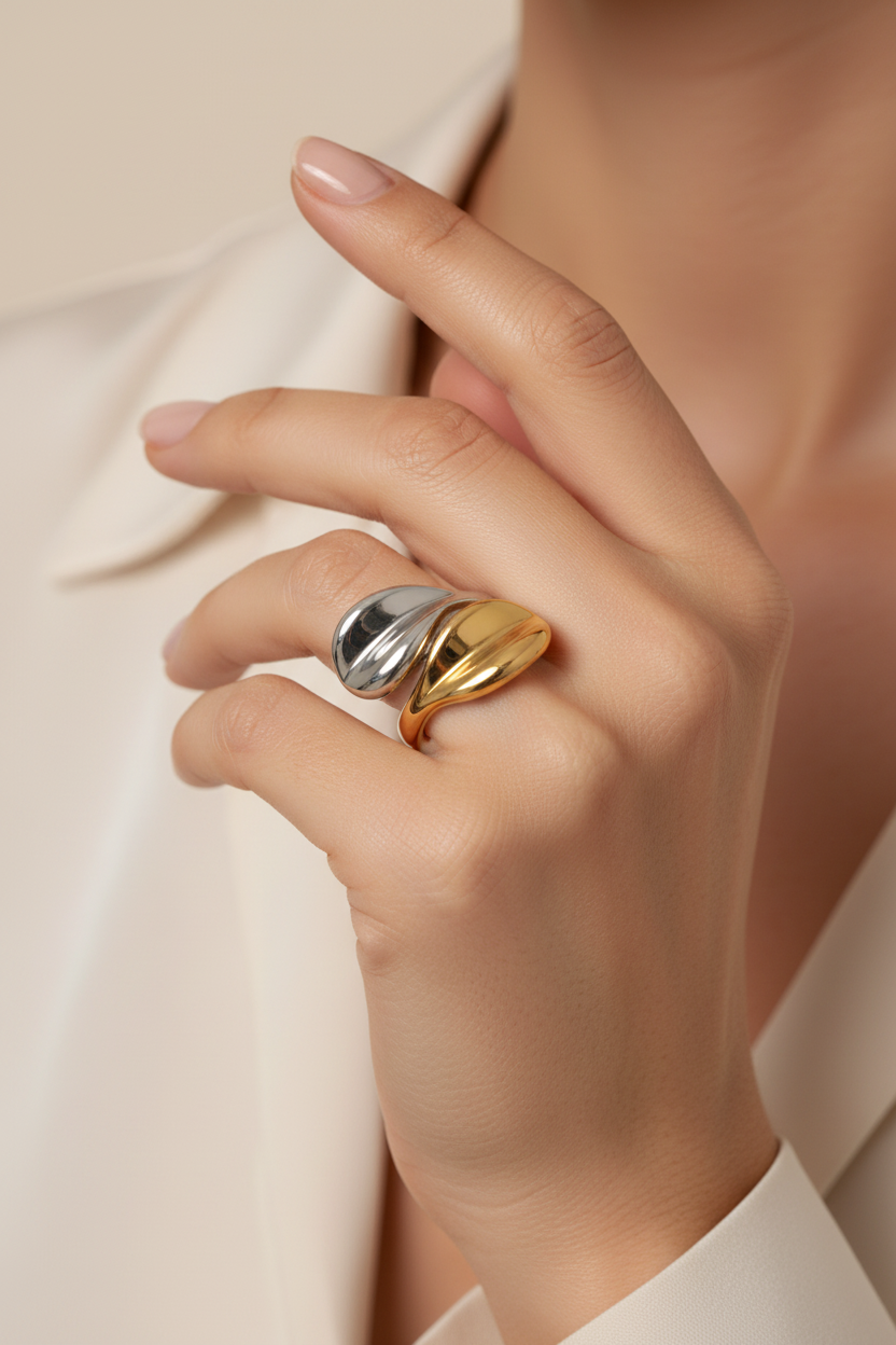Hand wearing a gold and silver ring on a neutral background